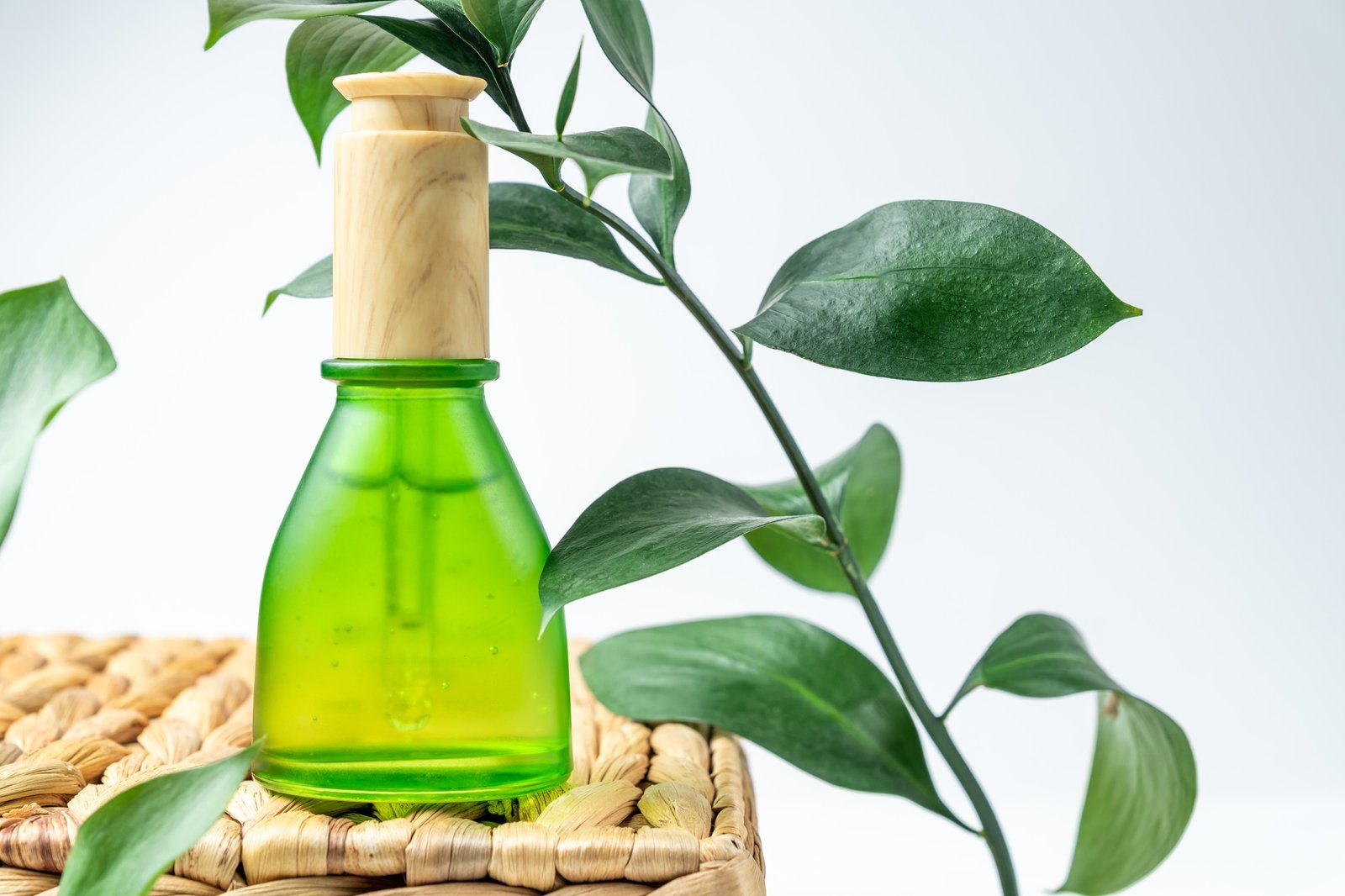 Green frosted glass cosmetic bottle with a dropper on a natural materials background